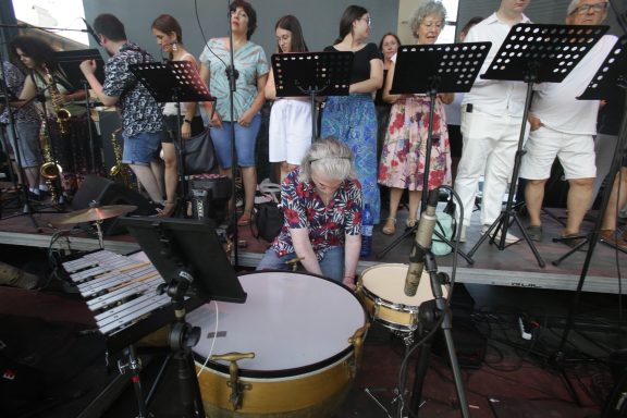 Músicos en un escenario, con una persona tocando instrumentos de percusión.